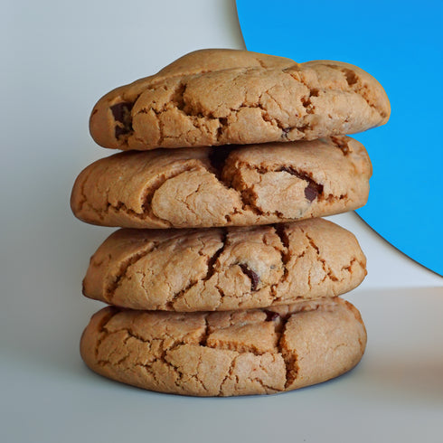 A stack of UniCookies chocolate chunk, The Regular Cookie, on a white backdrop with a pastel blue vinyl disc in the background.